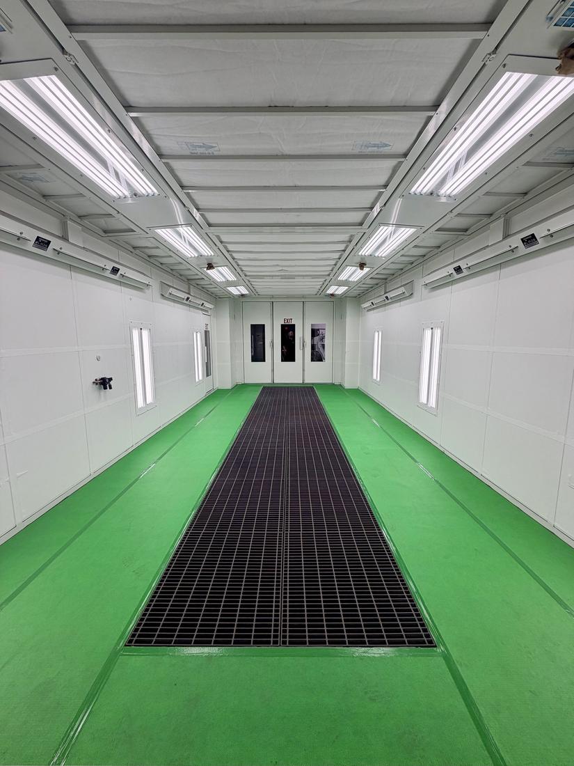 A freshly cleaned and painted downdraft spray booth with bright white walls and a green floor